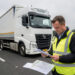 Camion de transport routier stationné sur une aire d’autoroute européenne, avec un conducteur vérifiant des documents de fret vierges et une carte d’itinéraire.