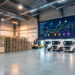 Centre logistique moderne avec palettes empilées, camions connectés, équipements de chargement et tableau numérique abstrait illustrant le suivi d’une livraison.