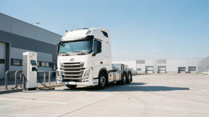 Tracteur routier électrique blanc de 44 tonnes en recharge rapide sur une aire logistique française, avec des bornes haute puissance sous un ciel bleu dégagé.